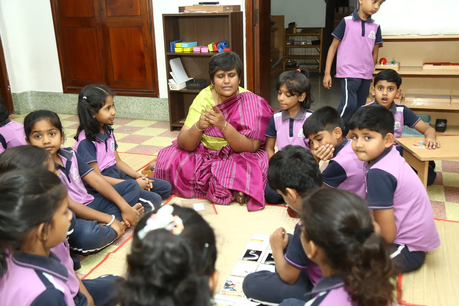 A Montessori guide leading circle time with children seated on the classroom floor