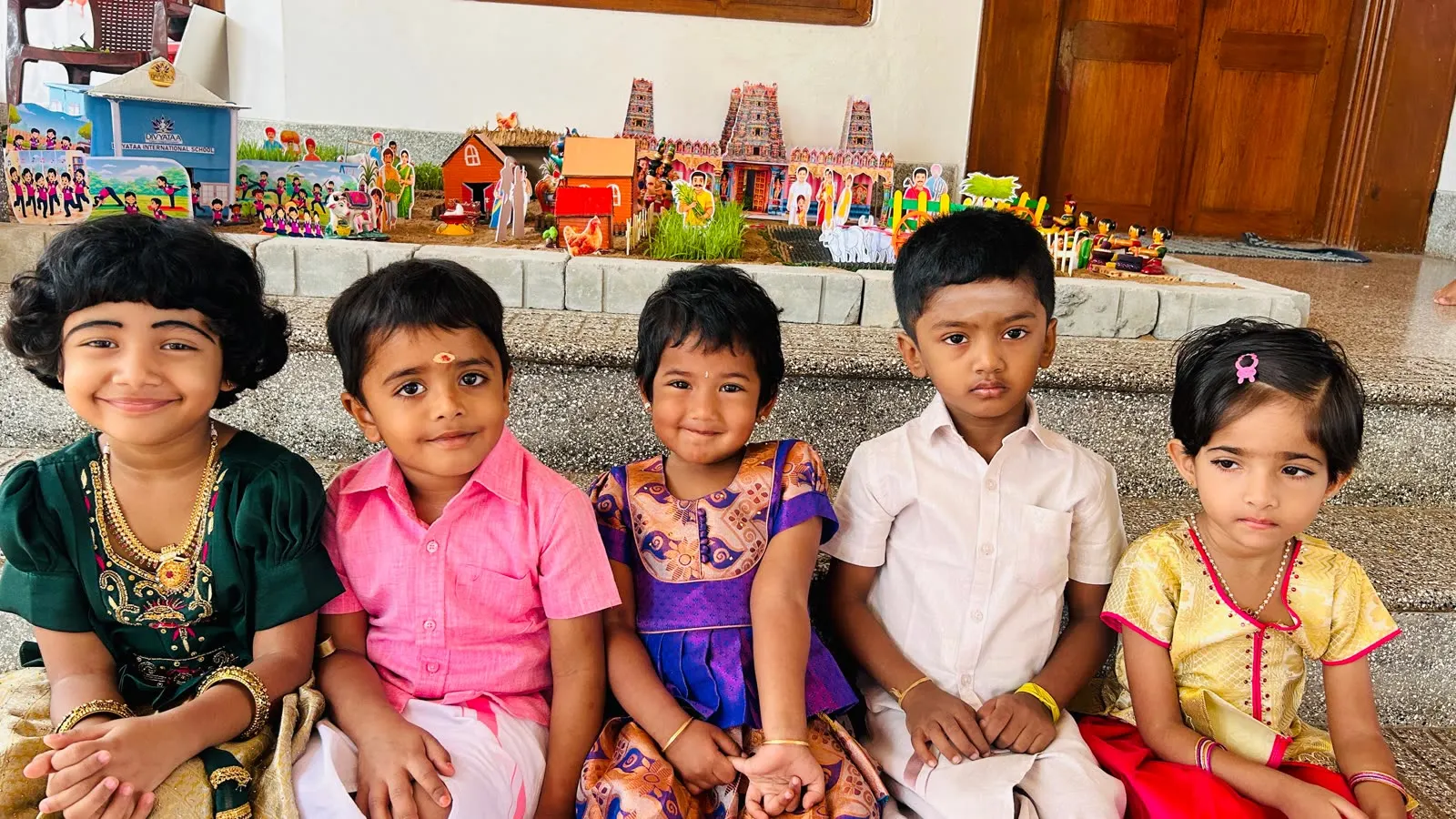 Children in festive clothes in front of a Navaratri golu display