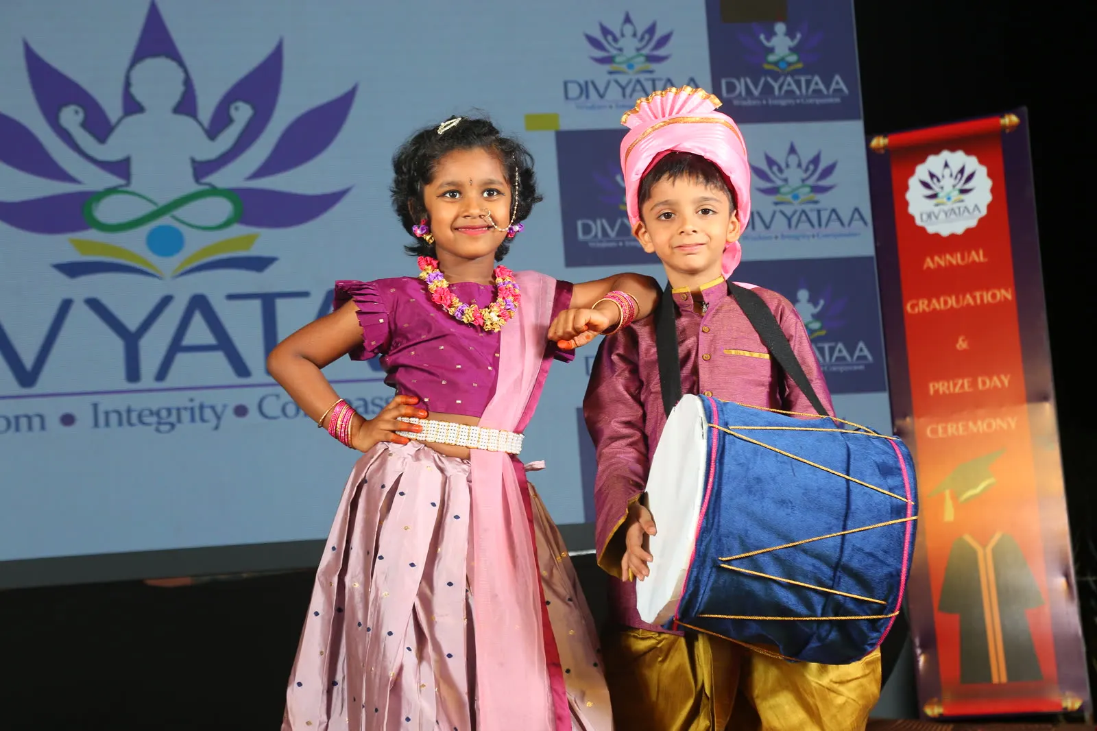 Two young performers posing with a drum on stage