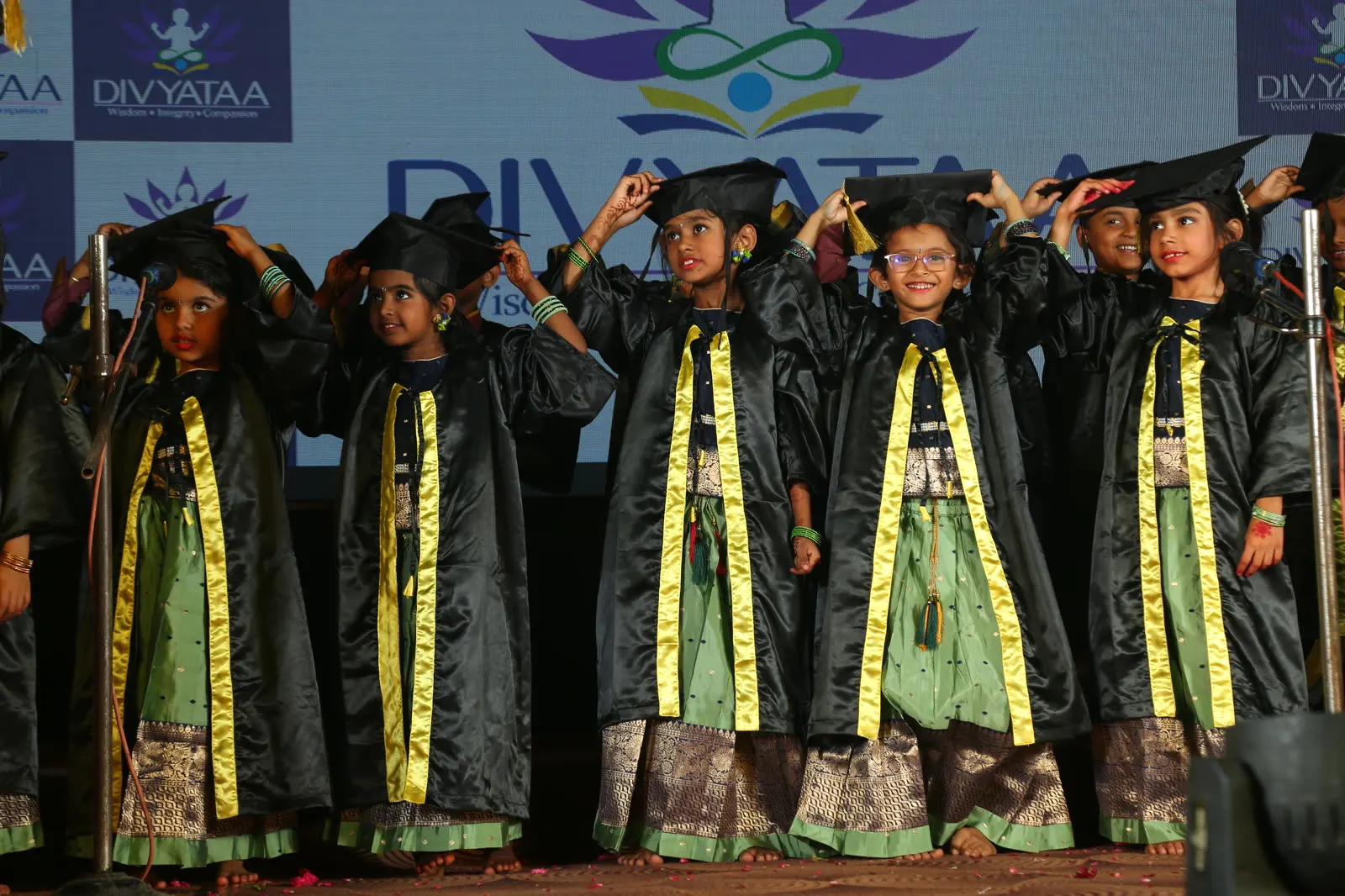 Graduating children in gowns adjusting their caps on stage