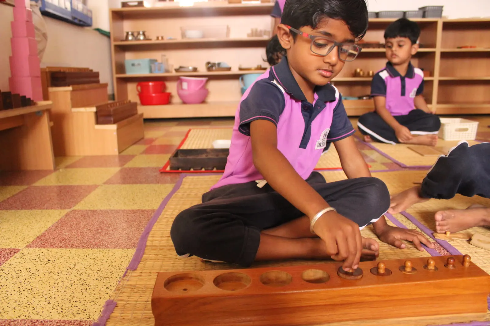 A child working with Montessori knobbed cylinders on the floor