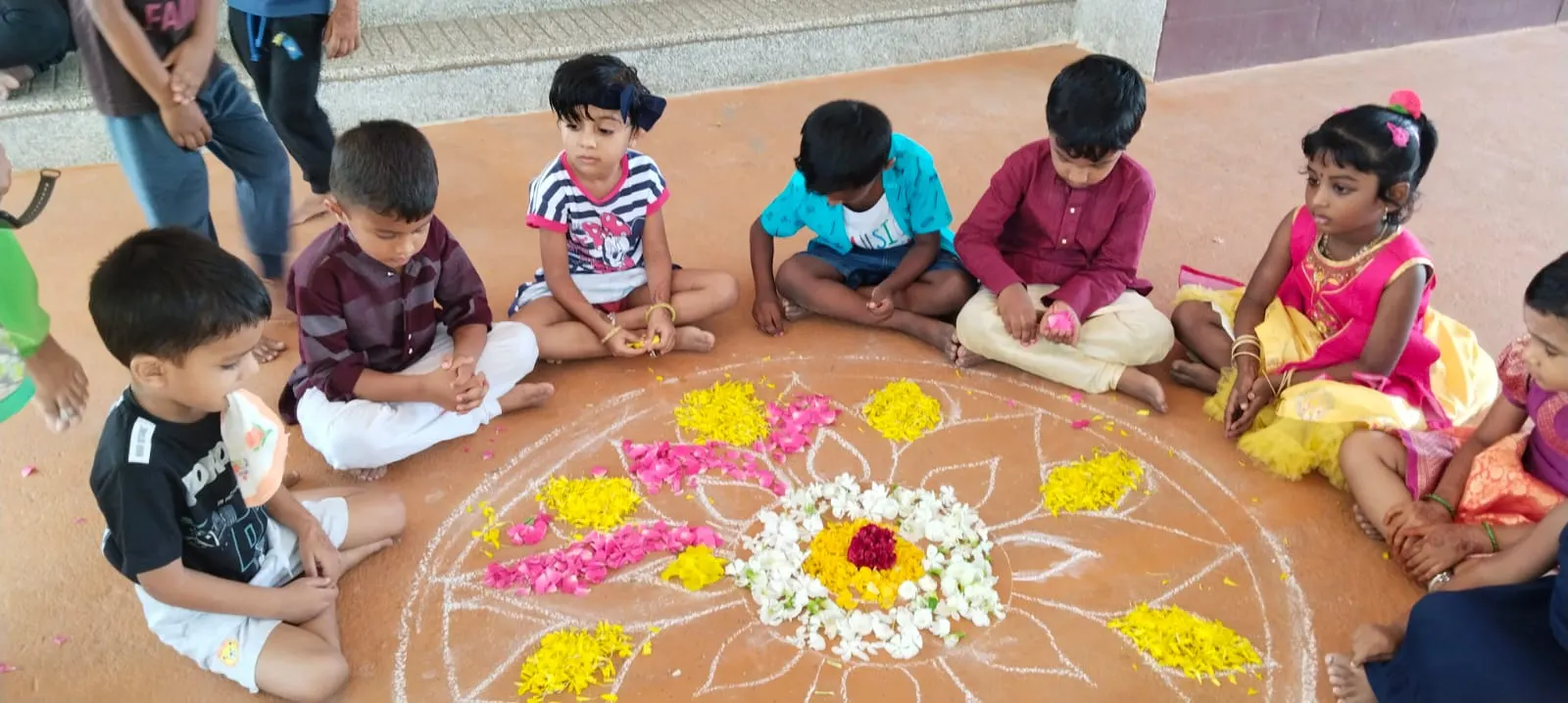 Children making a flower pookolam together on the floor