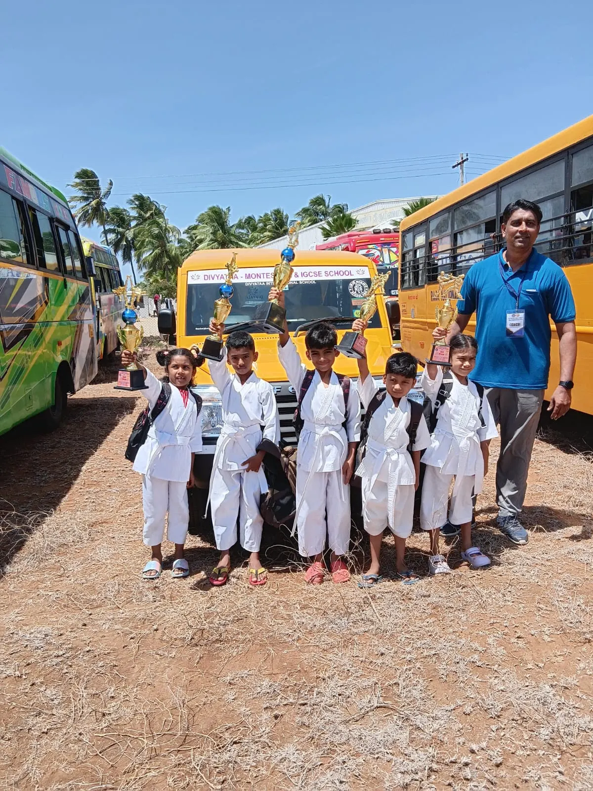 Karate champions raising their trophies beside the school bus
